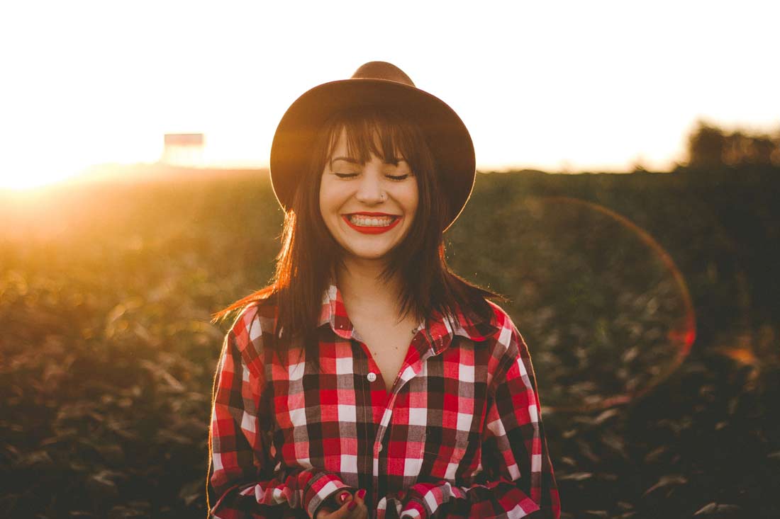 Finding your higher purpose in life will leave you with an unshakeable smile on your face. Image of a beaming woman with the sunset in the background.