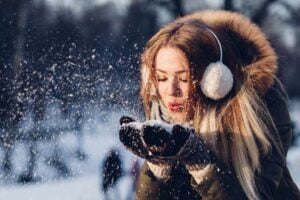 This winter, beat the blues and enjoy the weather. Image of a woman blowing snow from her hands.