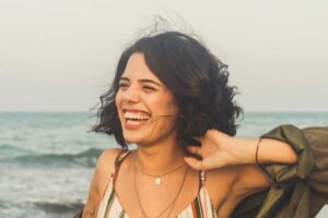Managing your thoughts and emotions can keep you glowing and happy. Image of a smiling woman on a beach.